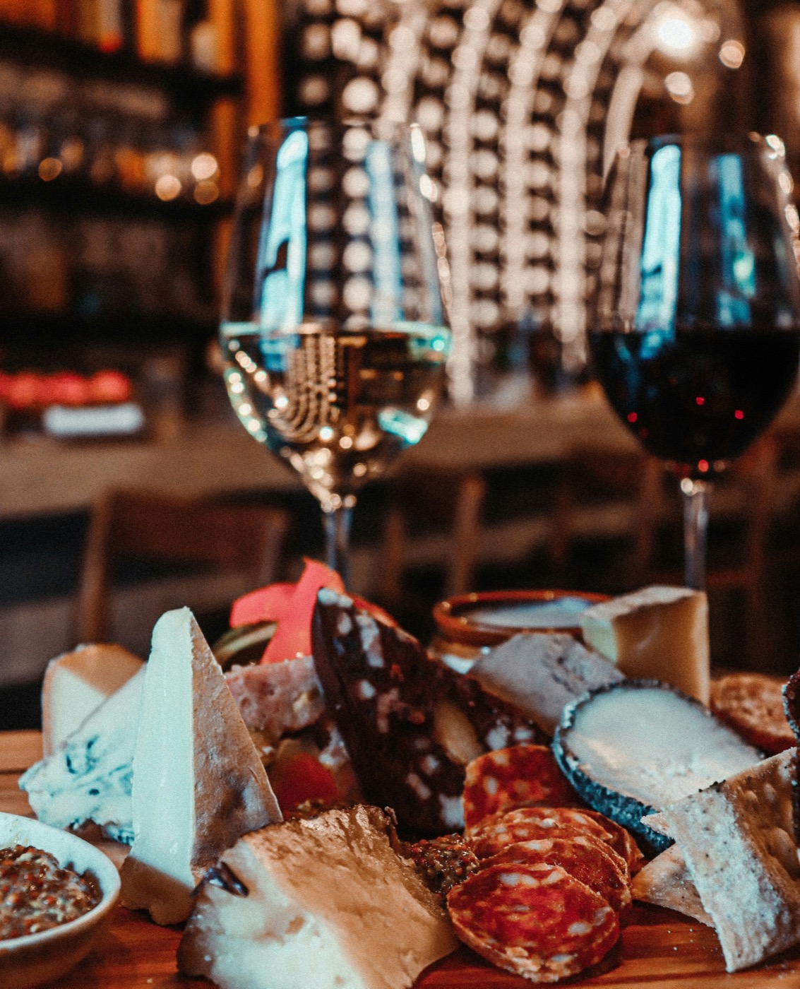 Wine glasses with a charcuterie and cheese board in a warm, candlelit setting