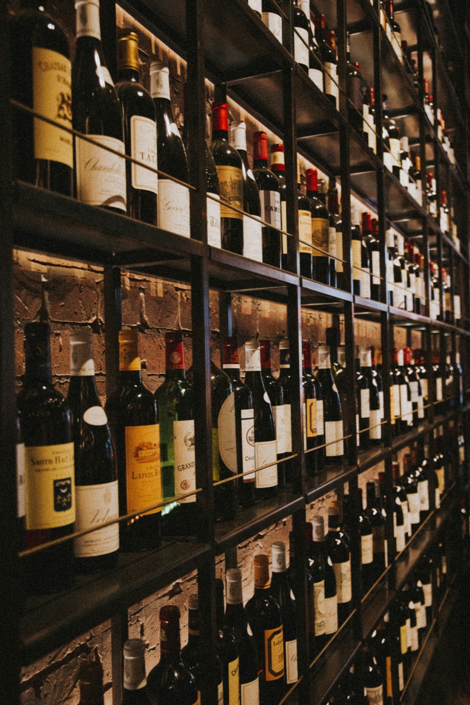 Wine cellar wall of bottles stacked floor to ceiling in atmospheric dark lighting
